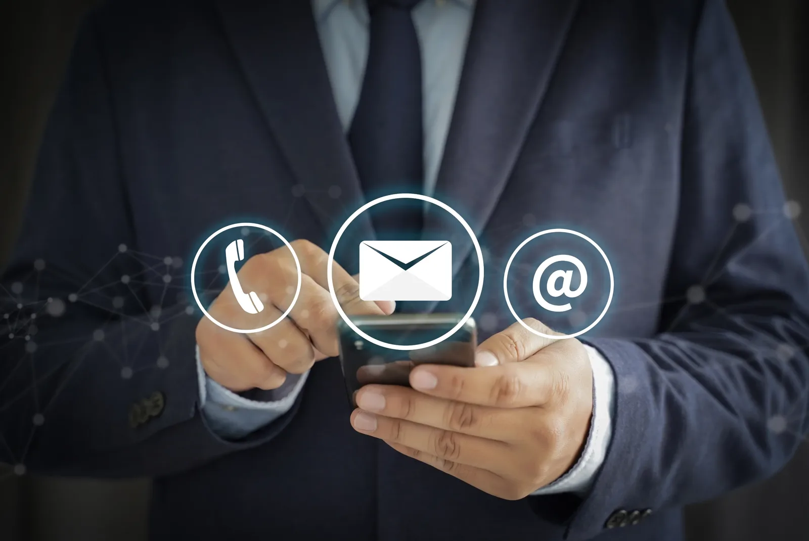 A person in a dark suit holding a mobile phone, with telephone, envelope and at-sign icons displayed in front.